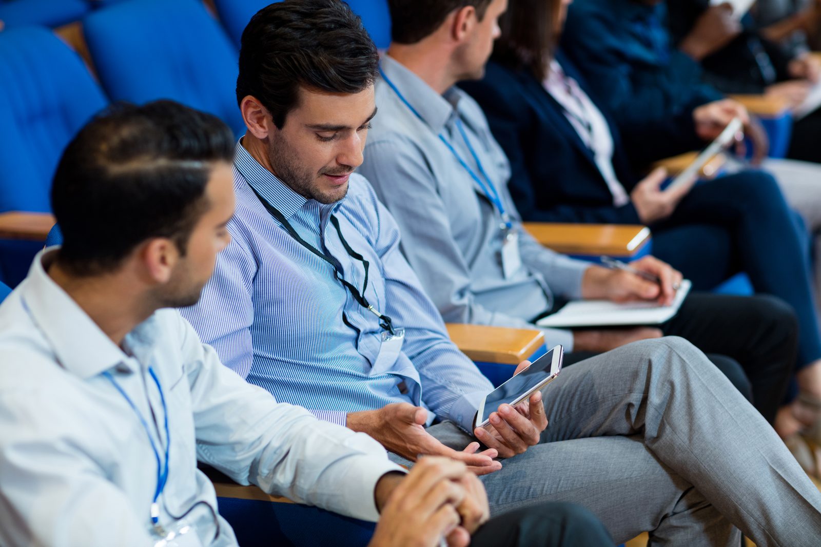 Business executives attending a tech conference session with tablets and notebooks